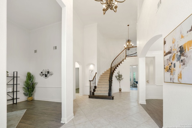 entrance foyer featuring arched walkways, a chandelier, stairs, and crown molding