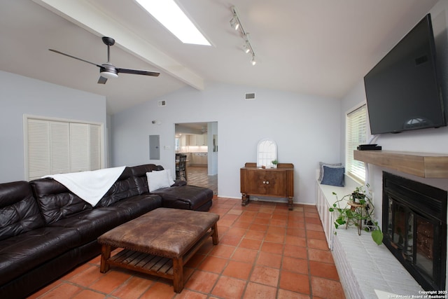 living area featuring visible vents, electric panel, a glass covered fireplace, vaulted ceiling with skylight, and ceiling fan