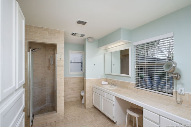 bathroom featuring visible vents, toilet, wainscoting, a stall shower, and tile walls