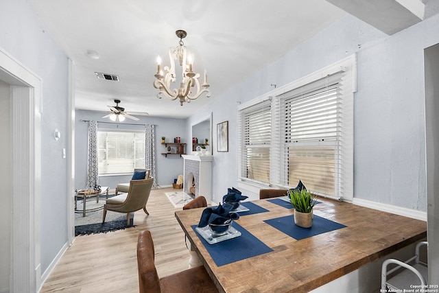 dining space featuring wood finished floors, visible vents, baseboards, a fireplace, and ceiling fan with notable chandelier