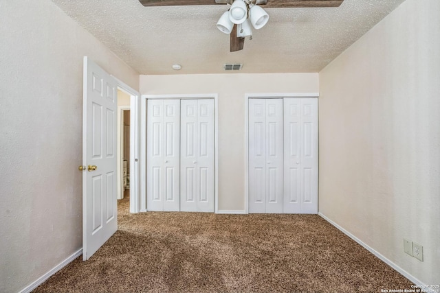 unfurnished bedroom featuring visible vents, carpet flooring, a textured ceiling, and two closets