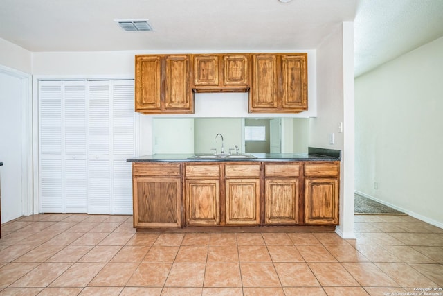 kitchen featuring visible vents, light tile patterned flooring, a sink, dark countertops, and brown cabinets