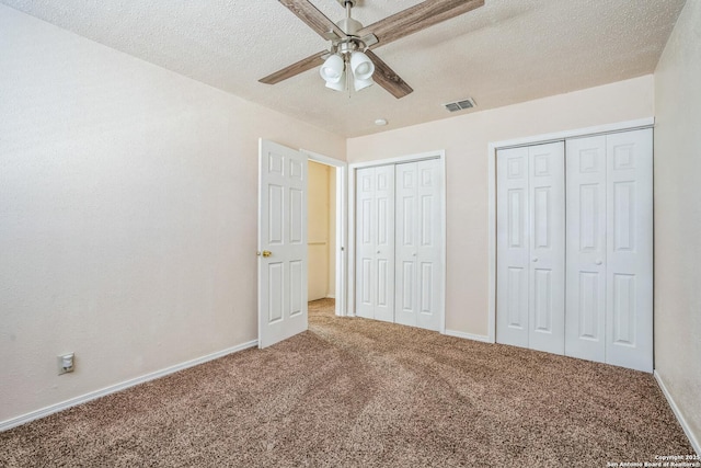 unfurnished bedroom with visible vents, a textured ceiling, two closets, and carpet