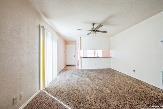 unfurnished living room featuring carpet floors, a sink, ceiling fan, a textured ceiling, and a textured wall