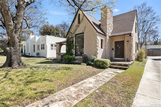 view of front of home with fence, a chimney, stucco siding, a front lawn, and stone siding