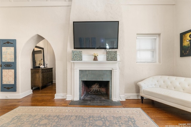 living room with arched walkways, a fireplace, baseboards, and wood finished floors