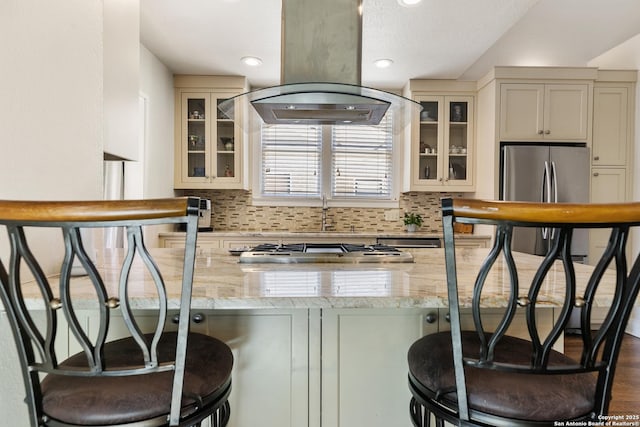 kitchen with tasteful backsplash, island exhaust hood, stainless steel appliances, and light stone countertops