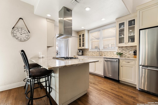 kitchen featuring dark wood-type flooring, a kitchen breakfast bar, island exhaust hood, a peninsula, and stainless steel appliances