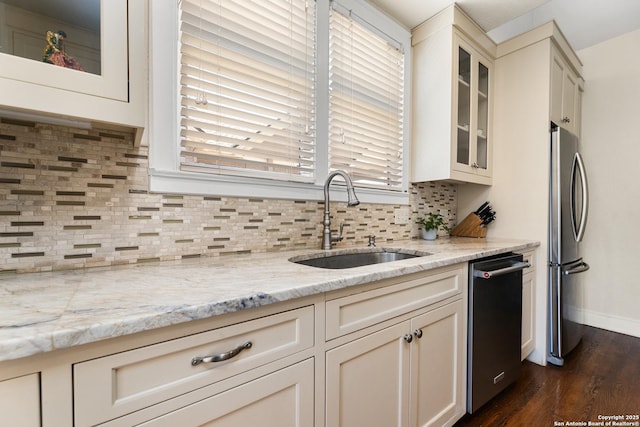 kitchen with a sink, light stone counters, tasteful backsplash, stainless steel appliances, and glass insert cabinets