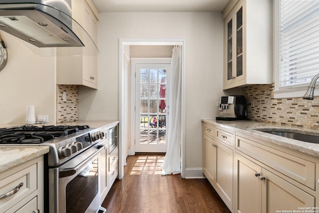 kitchen featuring a sink, backsplash, wall chimney exhaust hood, glass insert cabinets, and gas range