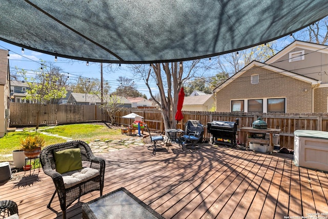 wooden terrace with grilling area, a lawn, and a fenced backyard