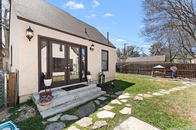 exterior space featuring stucco siding, a lawn, fence, french doors, and roof with shingles