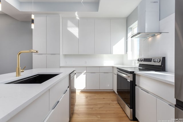 kitchen featuring backsplash, wall chimney range hood, light wood-style floors, stainless steel appliances, and a sink