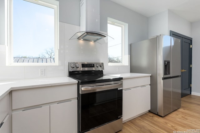 kitchen featuring island exhaust hood, stainless steel appliances, light wood finished floors, and light countertops