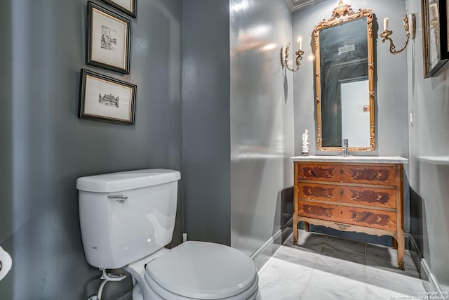 half bathroom featuring marble finish floor, toilet, vanity, and baseboards