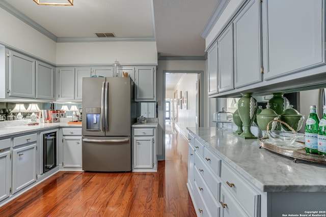 kitchen featuring beverage cooler, stainless steel refrigerator with ice dispenser, light stone counters, wood finished floors, and crown molding