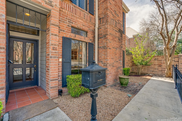 view of exterior entry featuring brick siding and fence