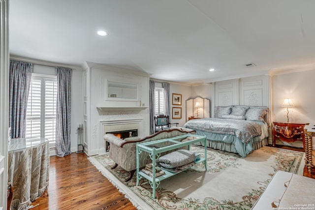 bedroom featuring multiple windows, ornamental molding, a lit fireplace, and wood finished floors