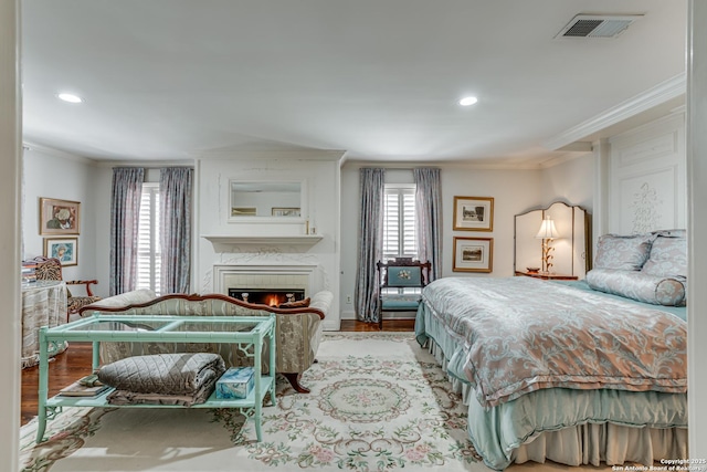 bedroom featuring visible vents, ornamental molding, wood finished floors, recessed lighting, and a lit fireplace