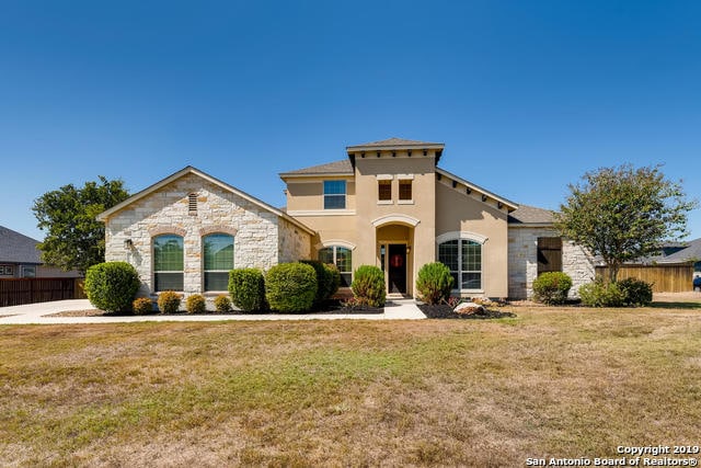 mediterranean / spanish-style house with stucco siding, stone siding, a front yard, and fence