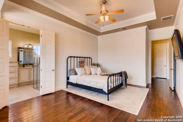 bedroom featuring visible vents, a raised ceiling, wood-type flooring, and ornamental molding