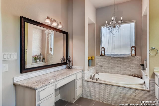 bathroom with a chandelier, tile patterned floors, vanity, and a bath