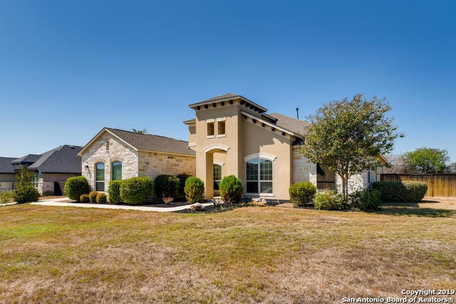 mediterranean / spanish house with a front yard, fence, stone siding, and stucco siding