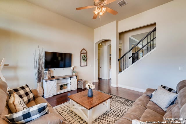 living area featuring visible vents, a ceiling fan, wood finished floors, arched walkways, and stairs