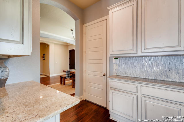 kitchen with arched walkways, dark wood-style floors, backsplash, and light stone countertops