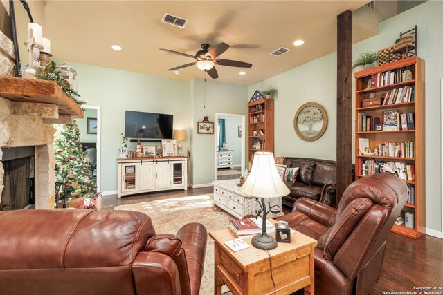 living area featuring a stone fireplace, ceiling fan, visible vents, and wood finished floors