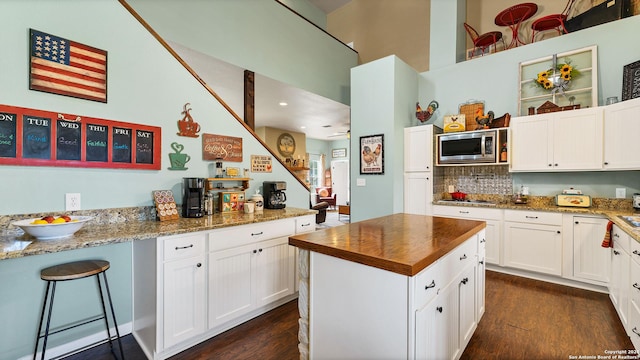 kitchen featuring dark wood finished floors, appliances with stainless steel finishes, white cabinets, decorative backsplash, and wooden counters