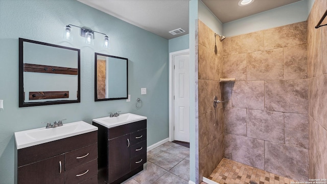 full bath with a sink, visible vents, tiled shower, and two vanities