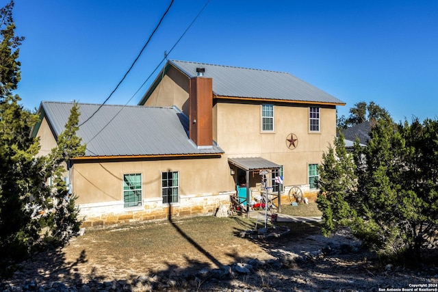 rear view of property with stone siding, stucco siding, and metal roof