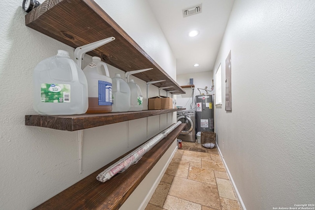 hallway with visible vents, stone tile floors, water heater, baseboards, and washer / dryer