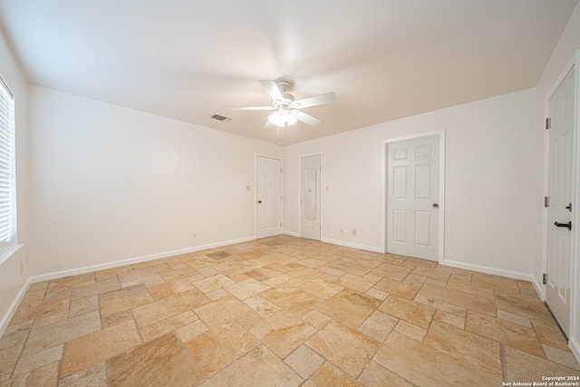 empty room with a ceiling fan, baseboards, visible vents, and stone tile flooring