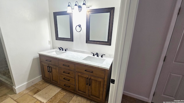 full bathroom featuring stone tile flooring, double vanity, baseboards, and a sink