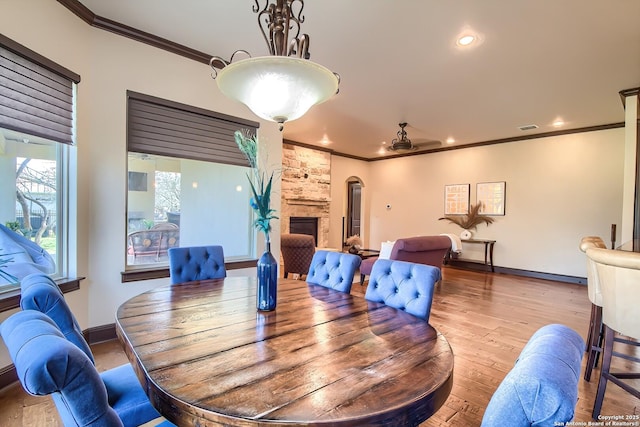 dining room with visible vents, ornamental molding, wood finished floors, a stone fireplace, and baseboards