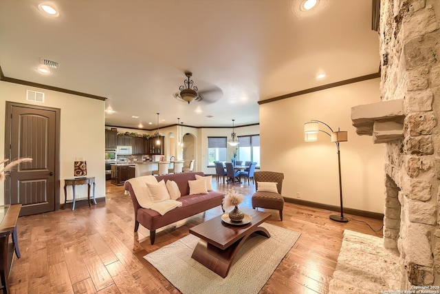 living room featuring light wood finished floors, visible vents, baseboards, and ornamental molding