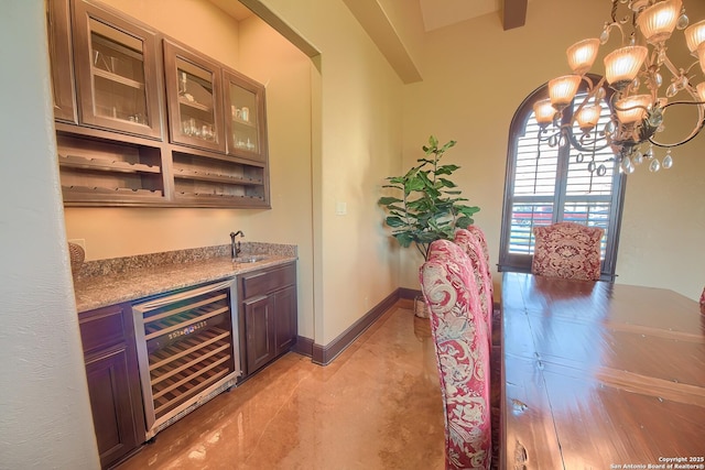 bar with baseboards, beverage cooler, indoor wet bar, a notable chandelier, and a sink