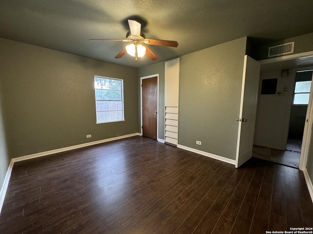 unfurnished bedroom featuring visible vents, a textured ceiling, a textured wall, and dark wood-style flooring