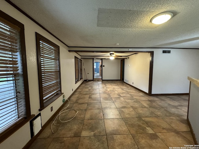 empty room featuring baseboards, visible vents, dark tile patterned flooring, ornamental molding, and a textured ceiling