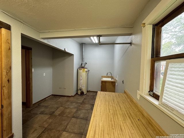 interior space with water heater, laundry area, a textured ceiling, and baseboards