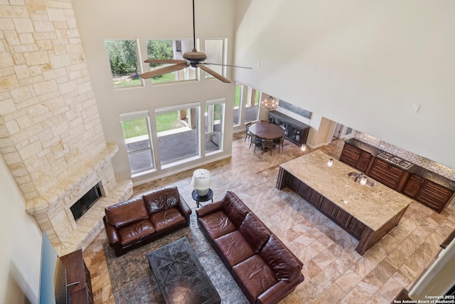 living area featuring a high ceiling, a stone fireplace, and ceiling fan