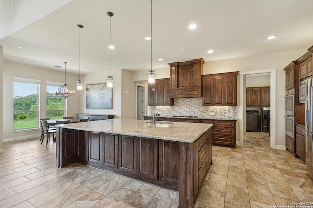 kitchen with a spacious island, separate washer and dryer, a sink, appliances with stainless steel finishes, and tasteful backsplash