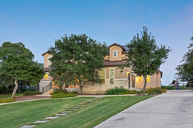 view of front facade with a front yard, metal roof, stone siding, and stucco siding