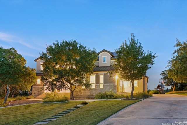view of property hidden behind natural elements with a front yard, a standing seam roof, stucco siding, stone siding, and metal roof
