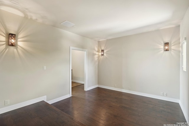 unfurnished room featuring dark wood finished floors, visible vents, and baseboards