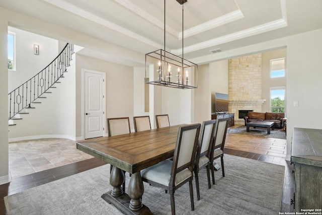 dining space with hardwood / wood-style floors, a stone fireplace, stairs, a raised ceiling, and a notable chandelier