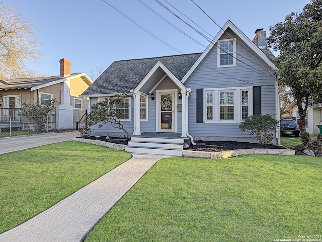 bungalow with a front lawn, fence, roof with shingles, and a chimney