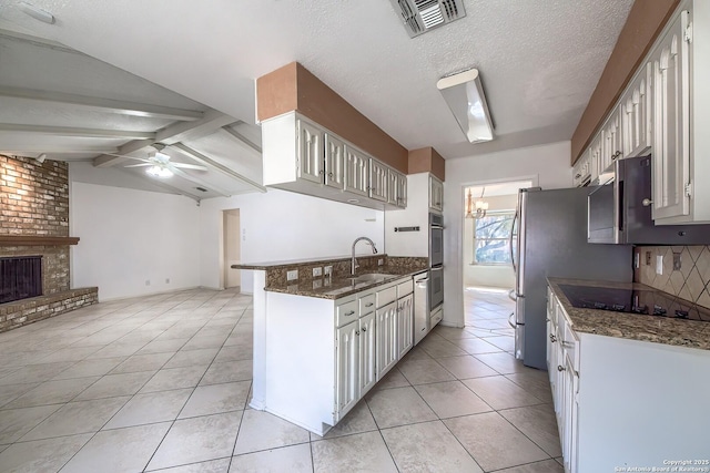 kitchen featuring lofted ceiling with beams, light tile patterned flooring, a sink, ceiling fan, and a brick fireplace